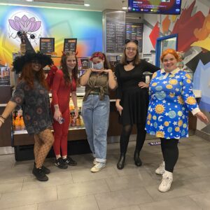 assistant manager and four baristas in halloween costumes posing in the dining room at the cafe