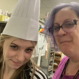 assistant manager wearing chef hat with manager in kitchen at the cafe