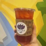 cold brew tea with lemonade in a cup with ice and a coffee sleeve with katora cafe logo that reads "have a great day!"